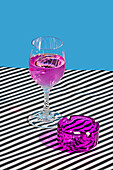Lila Cocktailglas, serviert auf einer gestreiften Stoffoberfläche mit einem lila Aschenbecher