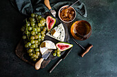Draufsicht auf verschiedene leckere Snacks mit Käse und serviert auf einem Teller, der auf einem Holzbrett mit Trauben, Feigen und Marmelade steht
