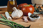 Fresh Mediterranean ingredients on a wooden board, including garlic, asparagus, and olives.