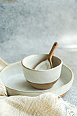 High angle of ceramic tableware set consisting of bowl and plate with wooden spoon placed near napkin on gray surface against blurred background