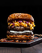 Nahaufnahme von Hamburger mit Makkaroni und Käse auf Holztablett auf dem Tisch vor dunklem Hintergrund platziert