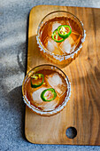 Top view of glasses with Japanese sochu liquor with mango juice and slices of Jalapeno pepper with salt on the glass edge placed on wooden table against blurred gray background