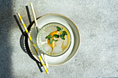 Top view of Summer cocktail with lemon vodka, slices of lemon and wild mint leaves with ice served on plate near straws on gray table