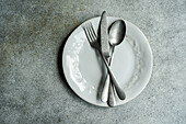 Top view of vintage cutlery set placed on white plate against gray surface in light kitchen