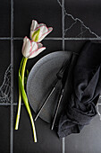 Top view of table setting with fresh tulip flowers on black concrete background