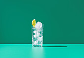 Ein klares Glas mit Gin Tonic und einer Limettenscheibe steht vor einem leuchtend grünen Hintergrund, der ein frisches und cooles Bild erzeugt