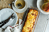 Top view of seasonal peach pie served on oven rack near plate with fork and knife and cup of tea placed on table near napkin