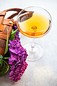 Blick von oben auf ein Glas mit einem frischen Getränk, das auf dem Tisch neben einem Strauß lila Hortensien in einem braunen Taschenkorb steht