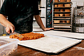 Anonymous mature baker dressed in casuals putting pastry delicious stuffing on dough at table while working in bakery kitchen