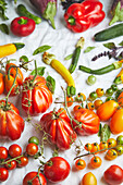 Draufsicht auf verschiedene frische, reife Gemüsesorten in Farbverläufen auf weißem Stoff auf einem Tisch