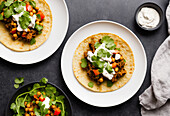 Top view of tasty tortilla flatbread with chickpea and meat topped with cilantro and sour cream served on plates over grey table background. Generative AI
