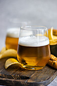 Tasty pieces of crisp potato chips in bowl with bread sticks and glasses of beer on wooden board placed over table in daylight