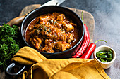 Traditional Georgian dish Ostri served in the bowl on wooden cutting board