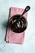 Heiße Schokolade von oben, serviert in einem transparenten Glas mit Löffel auf einer Serviette vor einer grauen Fläche