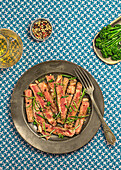 From above delicious sliced roast beef tagliatta served on plate near bowl with broccoli and herbs placed on patterned table towel