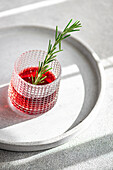Top view of elegant cocktail with cherry and apple juice mixed with vodka garnished with a fresh rosemary sprig presented on a circular tray