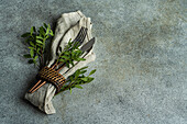 Hoher Winkel der Tischdekoration mit frischer Pistazienpflanze auf grauer Oberfläche mit Serviette und Besteck