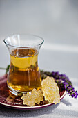 Closeup of glass of floral tea with fresh herbs served on ceramic plate against gray background
