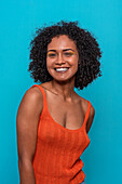 Portrait of slim African American female model in casual clothes with dark curly hair looking at camera against blue background