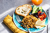 High angle of five ingredients lunch set consists of homemade goat cheese, fresh gucumber and tomato with leaves of basil herb, in addition to fried rice with meat with slices of healthy sour dough bread served with glass of carrot-apple juice against gray background