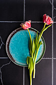 Draufsicht auf einen gedeckten Tisch mit frischen Tulpenblüten auf schwarzem Betonhintergrund