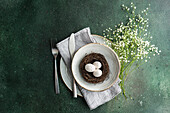 An artistic spring table setting featuring a bird's nest with speckled eggs, placed within layered crockery and accompanied by a delicate bouquet of baby's breath