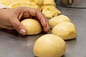 Anonymer schwarzer Bäcker, der rohen runden Brotteig aus einem Klumpen gemischten Mehls auf einem Metalltisch in einer modernen Bäckerei herstellt