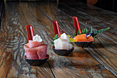 Row of dip bowls with served raw tuna and salmon white fish on wooden surface