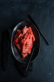 Top view of pieces watermelon on a black plate placed on a dark concrete background