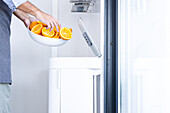 Side view of Anonymous crop male chef in apron and folded sleeves while standing putting squeezed orange fruits waste with hand into automatic trash bin from ceramic bowl in daylight