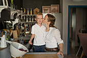 Loving Caucasian mid adult mother kissing cute adorable son on cheek while standing and cooking together in kitchen during weekend