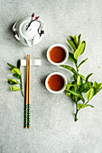 Top view of tea set in Asian style with lemon leaves and chopsticks against gray background