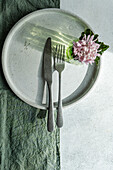 A top-down view of a chic table setting featuring a plate, cutlery, and a fresh flower on a textured cloth.