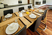 A modern dining room setup with a wooden table, ceramic dishes, and leather chairs, complemented by a sleek fireplace and hardwood flooring