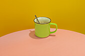 Green cup of hot aromatic coffee with spoon placed on pink round table against yellow background