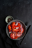 Schüssel mit Salat mit Bio-Tomaten vom Bauernhof und roten Zwiebeln mit Leinsamen und Meersalz auf schwarzem Hintergrund