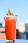 Glass of cold refreshing sex on the beach cocktail with ice cubes and orange slice placed against blurred