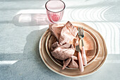 Ein elegant gedeckter Ostertisch mit pastellfarbenen Tellern, einer rosa Serviette und abgestimmtem Besteck, wobei eine sanfte Beleuchtung für eine heitere Atmosphäre sorgt