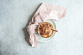 Top view of glass cup with coffee cream dessert with chocolate powder and ice served on plate with spoon on napkin for refreshing summer meal against blurred background