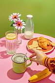 Unrecognizable person drinking hot aromatic coffee in cup placed on table with delicious croissants and banana decorated by flowers in vase