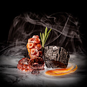 Appetizing octopus tentacles with green rosemary sprig and sauce placed near piece of wood on black surface in smoke