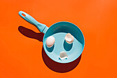 Blue frying pan with egg and eggshell on orange background