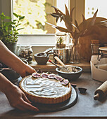 Woman hand holding homemade cheesecake with figs at kitchen background with window and natural light. Baking delicious cake at home with fruit and cream. Front view.
