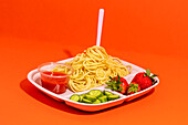 From above composition of spaghetti with fork tomato sauce cucumber slices and yummy fresh strawberries served for school lunch on red top table