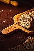 Hoher Blickwinkel auf köstliches, frisch gebackenes Brot mit knuspriger Kruste, bestreut mit einer Mischung aus Samen und auf einem Holzbrett platziert