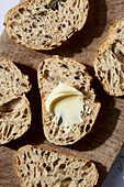 Nahaufnahme von frisch gebackenen, handwerklich hergestellten Brotscheiben, eine mit einem Stück Butter, auf einem hölzernen Schneidebrett mit schattigem Hintergrund angeordnet