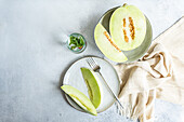 From above of green melon split in half placed in bowl and on plate with a lemonade on a concrete background