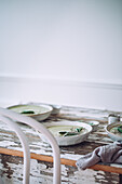 Ceramic bowls of green cream soup with sage served with seeds and herbs on wooden table with shabby surface against white background