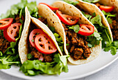 Appetitliche mexikanische Tacos mit scharfen Chilischoten und Koriander auf einem Teller mit grauem Hintergrund. Generative KI