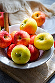 Top view of collection of ripe, colorful apples presented on a rustic wooden board, with a white plate, fork, and draped fabric creating a serene kitchen setting